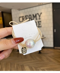 Detailed close-up of a pearlescent aurora bead on a cream double-strand elastic hair tie