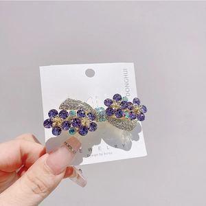 Detailed macro view of purple rhinestone flower bowtie hair clip on white card