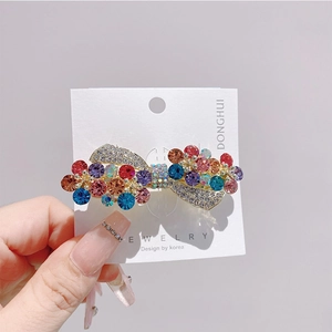 Detailed close-up of a bow hair clip with colorful rhinestones on a gold alloy base