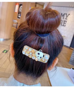 Vue détaillée d'une pince à cheveux dorée carrée avec strass, perles et tête de panda