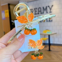 Detailed close-up of golden metal hair clips featuring orange enamel maple leaves and persimmons