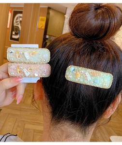 Dettaglio di fermagli per capelli con fiori di conchiglia, perle e strass rosa e verdi