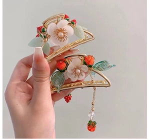Detail of golden hair claws with white flowers and red strawberry pendant charms