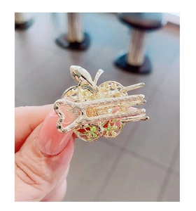 Detalle de una pinza para el cabello pequeña con forma de manzana dorada y asa de corazón