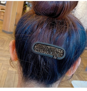Detailed view of an oval black hair clip with sparkling rhinestones on braided hair