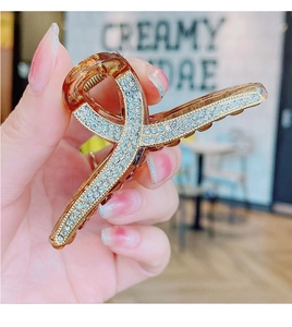 Close-up of amber resin hair claw clip with cross design and inlaid white rhinestones