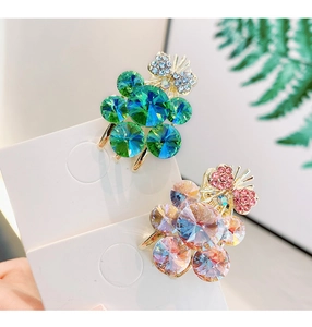 Detailed close-up of crystal flower hair clips in green and pink on card packaging