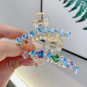 Due fermagli per capelli trasparenti con cuori di strass colorati in mano a una donna