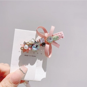 Detailed close-up of a pink ribbon bow hair clip with crystal and pearl embellishments