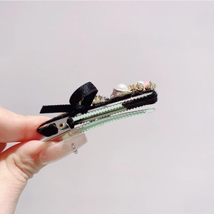 Detailed close-up of a black satin bow hair clip with pearls and sparkling crystals