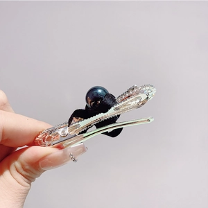 Détail d'une barrette à nœud argentée avec strass brillants et une perle noire