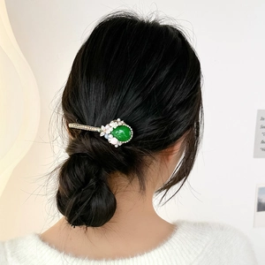 Baroque hair clip with emerald cat eye stone, pearls, and flowers on a low bun hairstyle