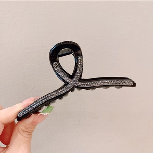 Dettaglio di un grande fermaglio per capelli nero con strass e design ad anello incrociato