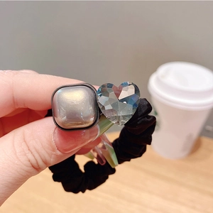 Détail d'un chouchou noir avec une perle carrée scintillante et un cœur en cristal clair