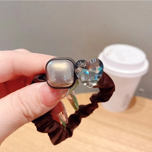 Détail de l'élastique marron foncé avec perle carrée dorée et charm de cœur en cristal