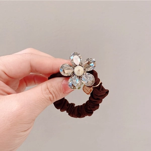 Détail d'un chouchou plissé marron avec breloque fleur en cristal et étiquette en métal