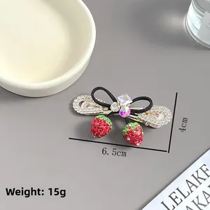 Détail de pince à cheveux fraise avec strass et nœud noir, taille 6,5cm par 4cm