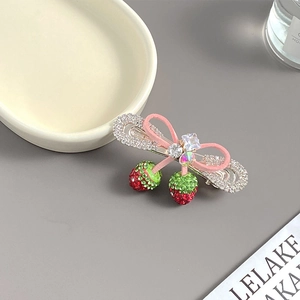 Détail de la pince à cheveux fraise avec nœud rose et strass sur un plateau en céramique