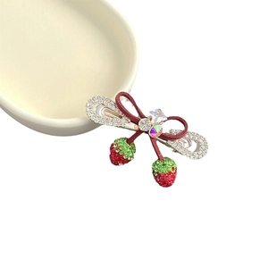 Pince à cheveux nceud fraise avec strass et cristaux posée sur une assiette blanche