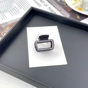 Gros plan d'une pince à cheveux rectangulaire noire ornée de strass gris foncé sur carte