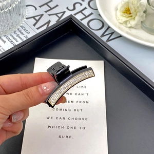 Elegante pinza per capelli nera con strass e finiture dorate tenuta in mano