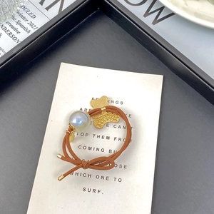 Detail of a brown elastic hair tie with a golden metal bear and iridescent pearl bead