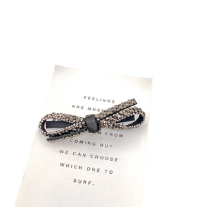 Elegant bow hairclip featuring dark grey rhinestones on a black fabric base, flat lay view