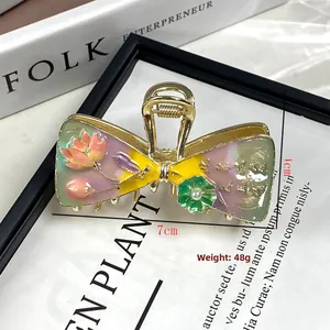 Dettaglio di un fermaglio a farfalla dorato con smalto floreale e perle retrò