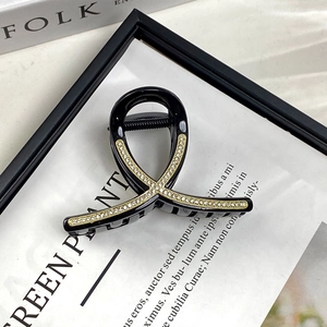 Close-up of a black cross ribbon hair claw clip with gold rhinestone strips on a desk
