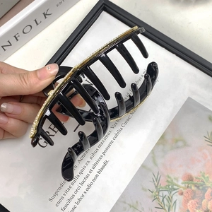 Macro detail of large black shark hair claw clip with gold rhinestone inlays on resin