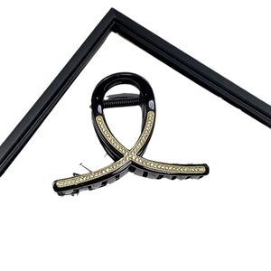 Elegant black criss-cross hair claw clip with sparkling rhinestones on a geometric stand