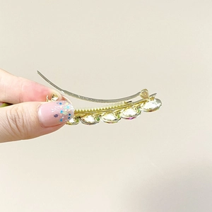 Macro shot of gold curved hair clip featuring colorful gradient crystals and branding