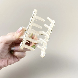 Detail showing creamy matte hair claw with crystal accents and gold spring mechanism