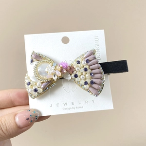 Close-up of beaded bow hair clip with purple stones, pearls and a pink rose detail