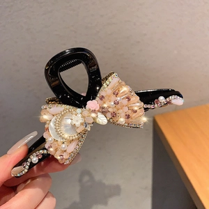 Close-up of handmade bow hair clip with pink beads, rhinestones and pearl flower details