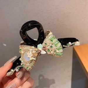 Detail of luxury hair claw featuring emerald rhinestones, pearls and a bow design