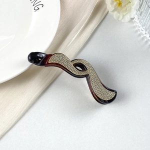 Dettaglio macro del fermaglio a banana tartarugato con strass lucidi su raso bianco