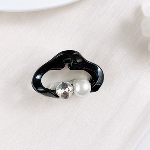 Close-up of a mini black hair claw clip with a large faceted crystal and white pearl