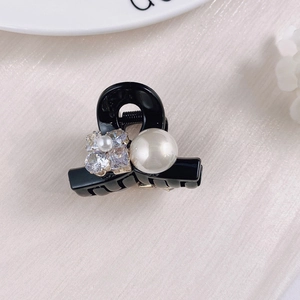 Detail of a mini black hair claw clip featuring a large pearl and rhinestone flower design