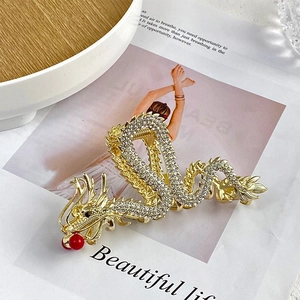 Detailed close-up of a golden dragon hair claw clip with rhinestones and red bead accents