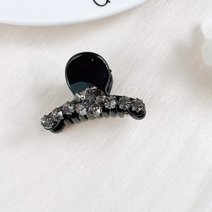 Detail of a mini black hair claw clip featuring elegant grey rhinestones on silk