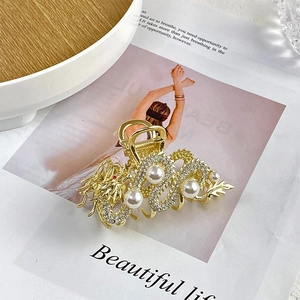 Close-up of golden dragon hair claw clip with inlaid rhinestones and pearls on a magazine