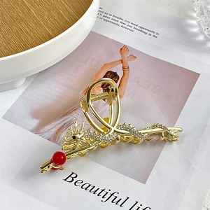 Detailed macro of golden dragon hair claw clip with rhinestones and red bead on a book