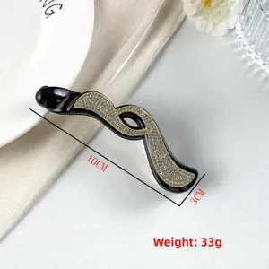 Dettaglio del fermaglio a banana da 10cm con strass dorati su base in resina nera