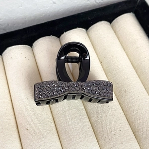 Close-up of black bow hair claw clip with rhinestones on a beige velvet display box