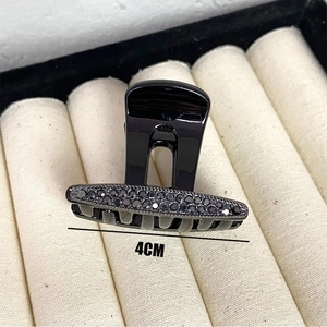 Detail view of 4cm black hair claw clip with rhinestones on cream textured lining