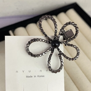 Detailed close-up of a flower-shaped hair clip with grey crystals on nyunyu card