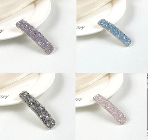 Detailed view of four crystal-encrusted hair clips in lavender, blue, grey, and pink