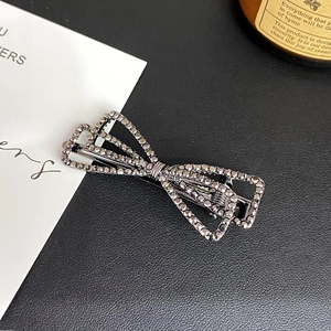 Detailed view of alloy bow hairpin with dark grey rhinestones on black leather background