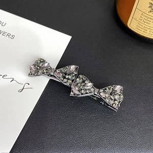 Detailed close-up of charcoal grey rhinestone bow hair clip on a premium leather texture